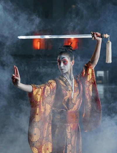 Dramatic samurai cosplay featuring a woman in kimono wielding a katana amidst smoke.