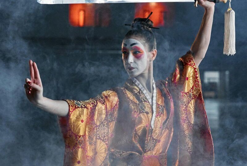 Dramatic samurai cosplay featuring a woman in kimono wielding a katana amidst smoke.