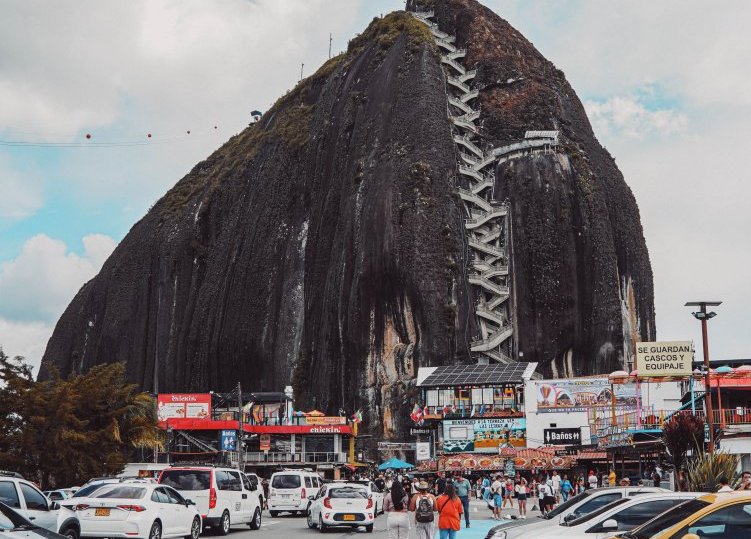 A captivating view of El Peñol Rock with cars parked around, showcasing the massive stone and its staircase path.