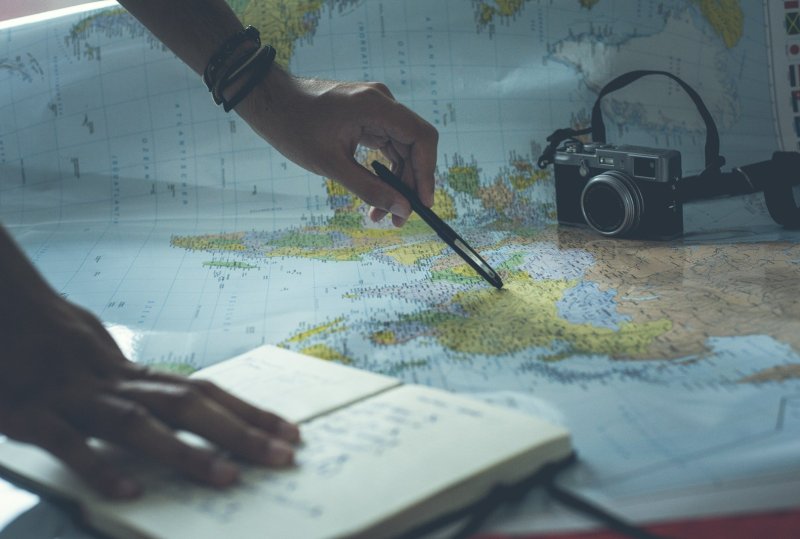 person pointing a pen on a map and writing on white paper